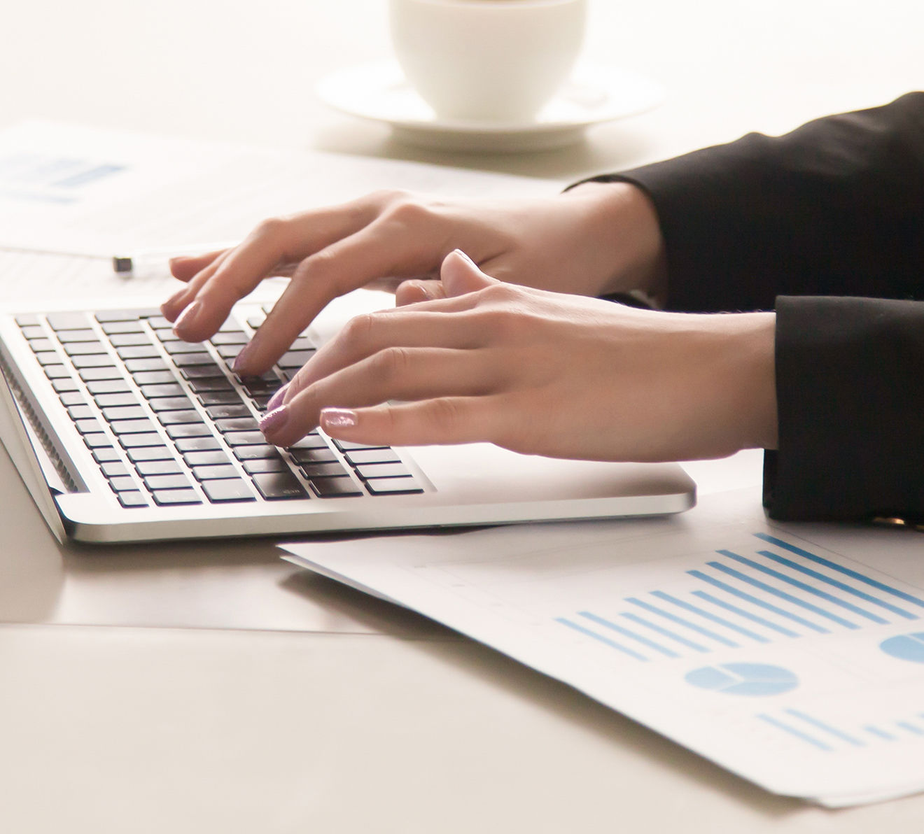 Hands typing on laptop with printed charts