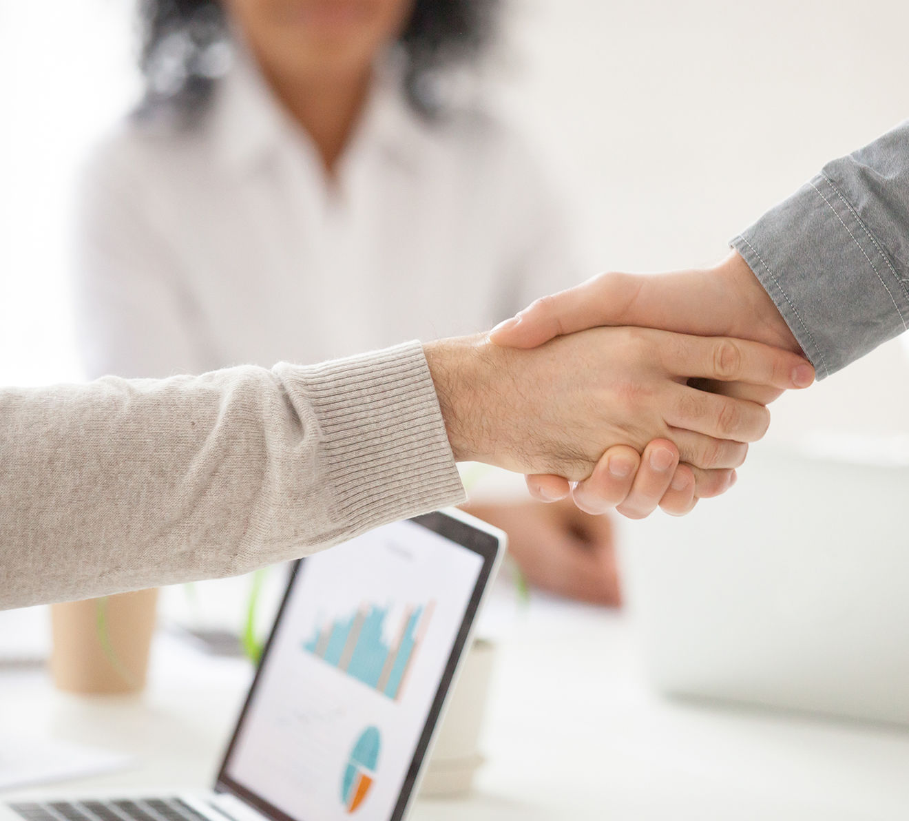 Business handshake over laptop with charts